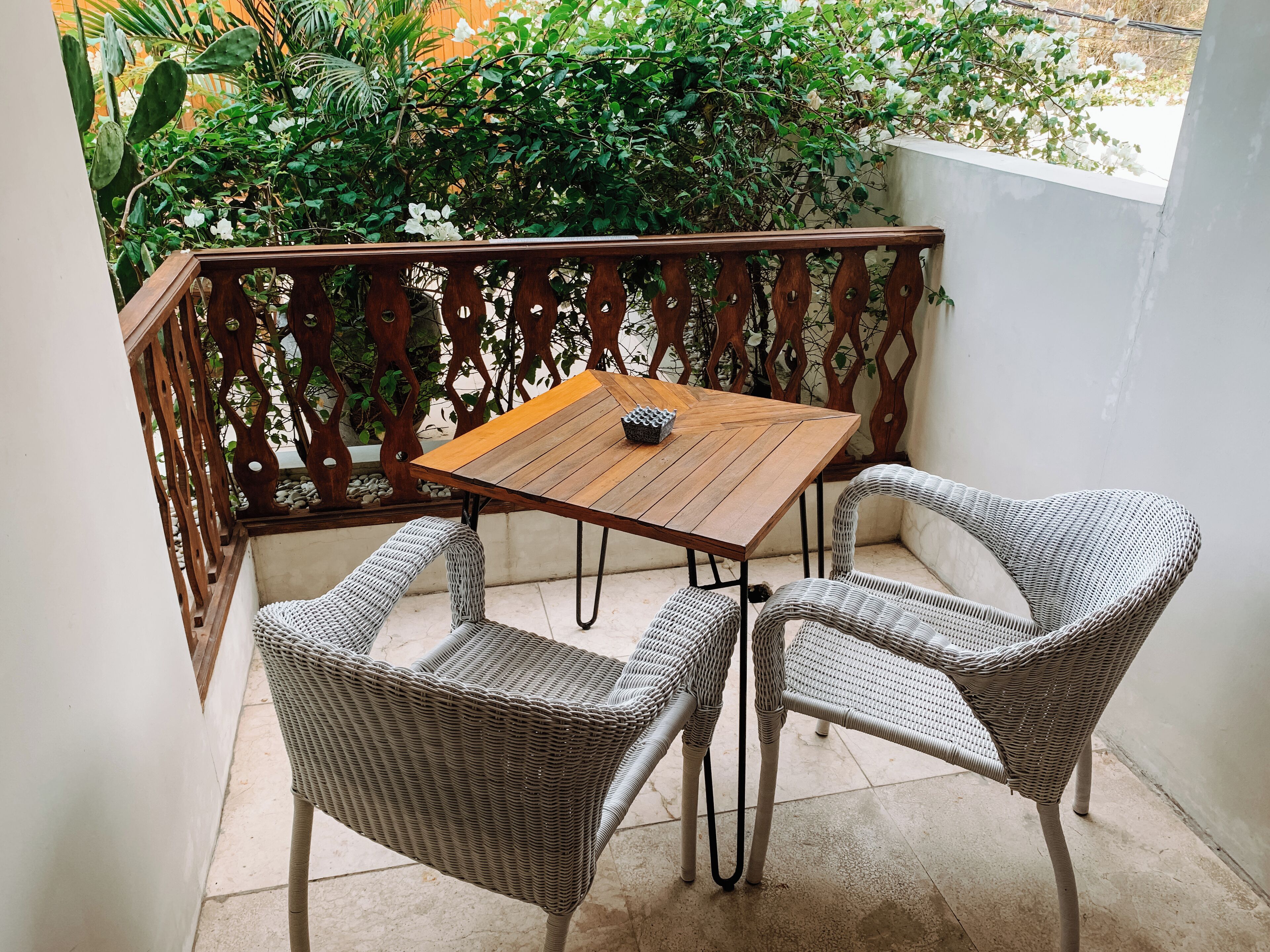 A balcony with wicker chairs and a wooden table.