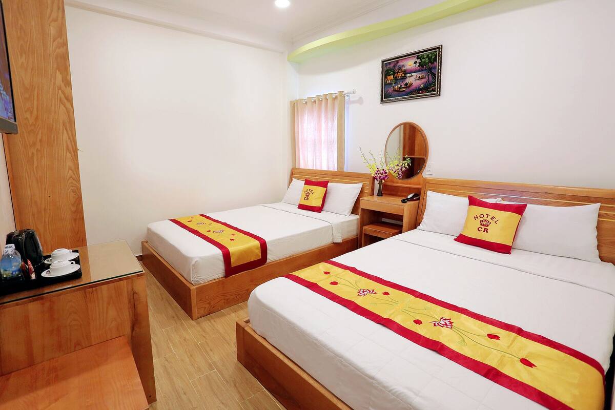 A hotel room with two beds, each with a red and yellow bedspread, a wooden headboard, a bedside table, and a mirror.