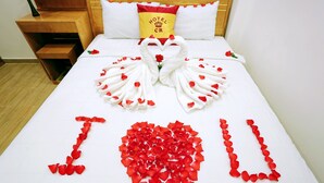 Una habitación de hotel con una cama decorada con pétalos de rosa y un arreglo con forma de corazón que dice 'Te amo'.