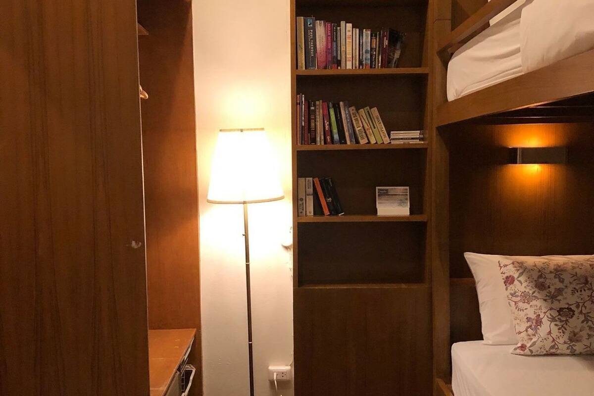 A compact room with a bunk bed, a bookshelf, a desk, and a lamp.