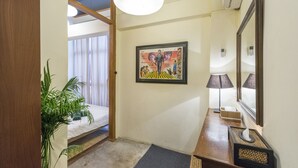 Un pasillo con puerta de madera, planta en maceta, cuadro en la pared, lámpara y espejo.