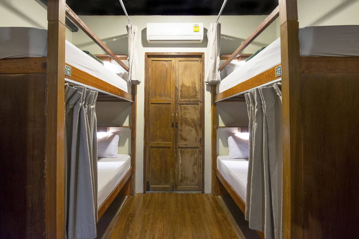 A narrow corridor with bunk beds on either side, a wooden door at the end, and an air conditioning unit above.