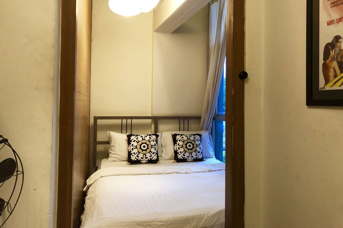 A bedroom with a bed, a ceiling light, a window with curtains, and a wall-mounted picture.