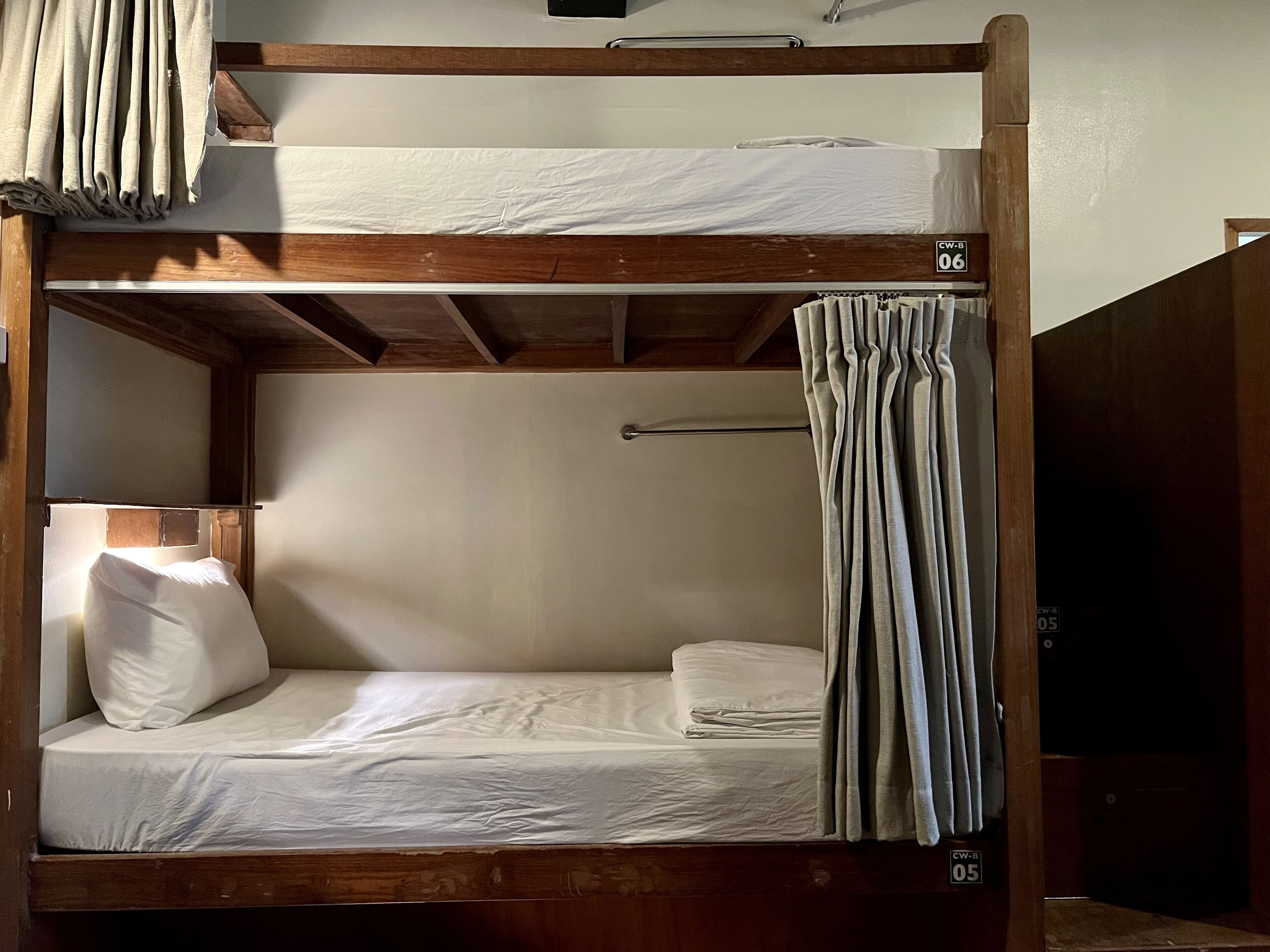 Una cama litera con dos niveles, cada uno con un colchón y almohadas. Hay una cortina en el lado derecho de la cama inferior.