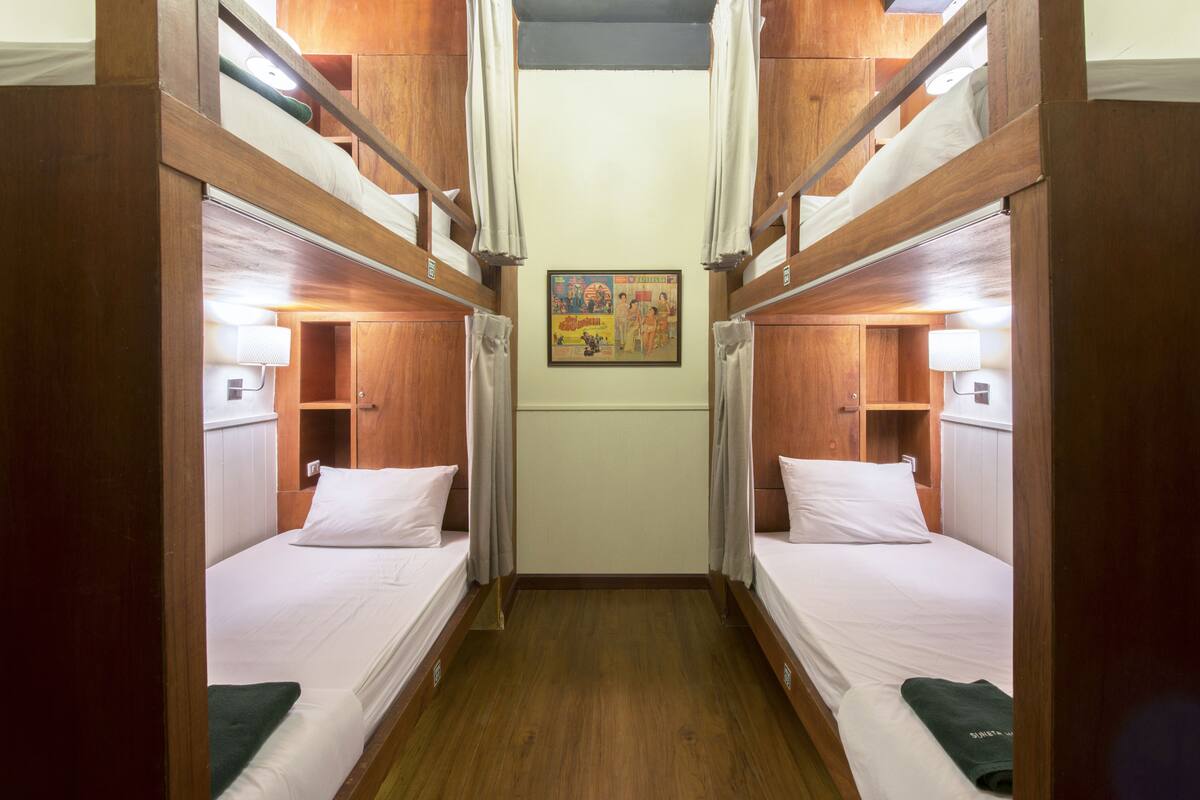 A narrow room with two bunk beds, wooden walls, a small shelf, and a framed picture on the wall.