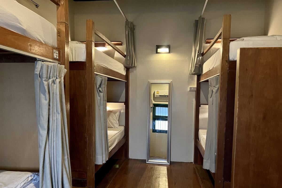A narrow corridor with bunk beds on either side, a mirror on the wall, and a small window at the end.