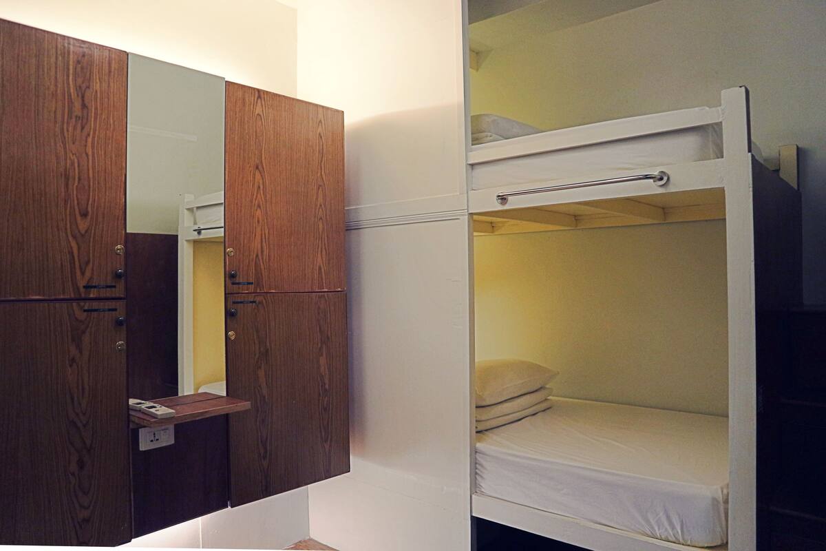 A bunk bed with a small shelf and a mirror above it, and a wooden wardrobe with a mirror.