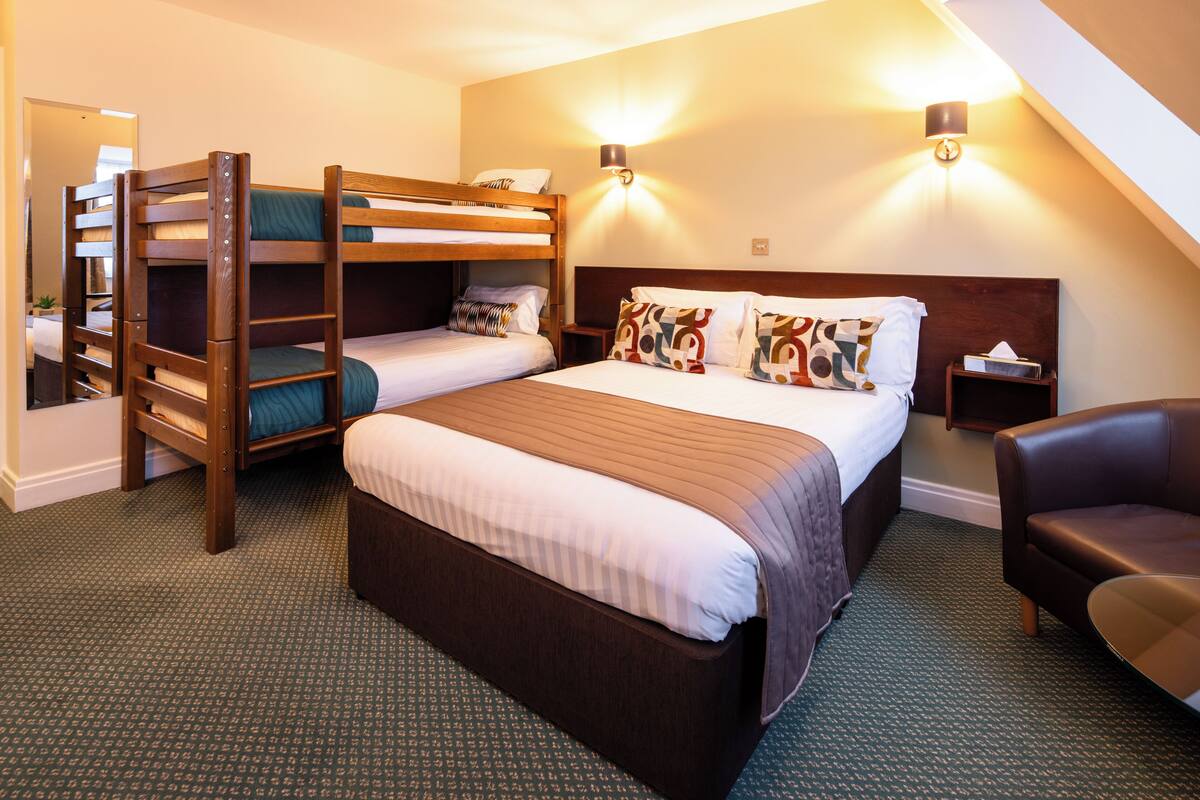 Een hotelkamer met stapelbedden, een groot bed, een stoel en twee wandlampen.