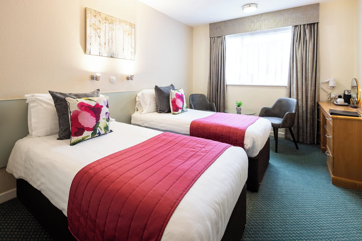 Een hotelkamer met twee bedden, een bureau, een stoel en een raam met gordijnen.