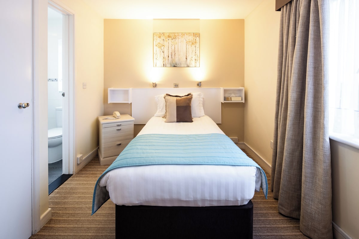 Hotelkamer met een bed, nachtkastjes, een kunstwerk aan de muur en een raam met gordijnen.