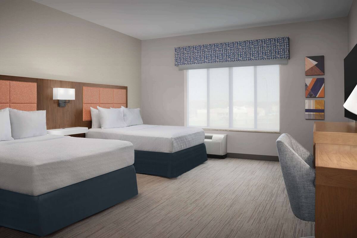 A hotel room with two beds, a desk, a chair, a large window with a view, and a wall-mounted TV.