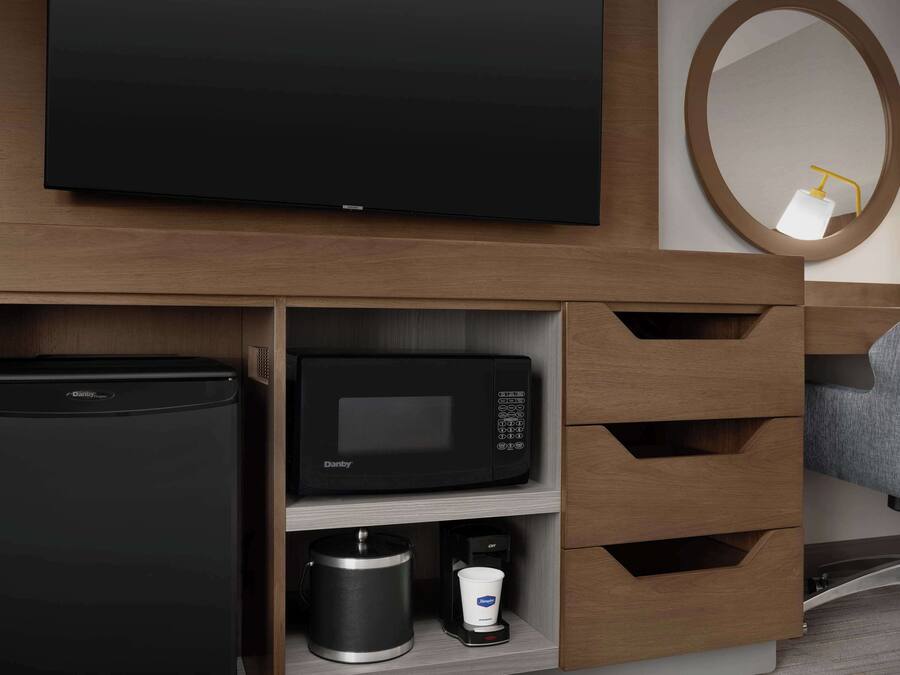 Habitación de hotel con televisión de pantalla plana, microondas negro, cafetera y refrigerador pequeño.