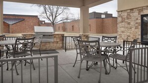 An outdoor patio with metal chairs and tables, a grill, and a stone wall. - Hampton Inn & Suites Williston (Williston)