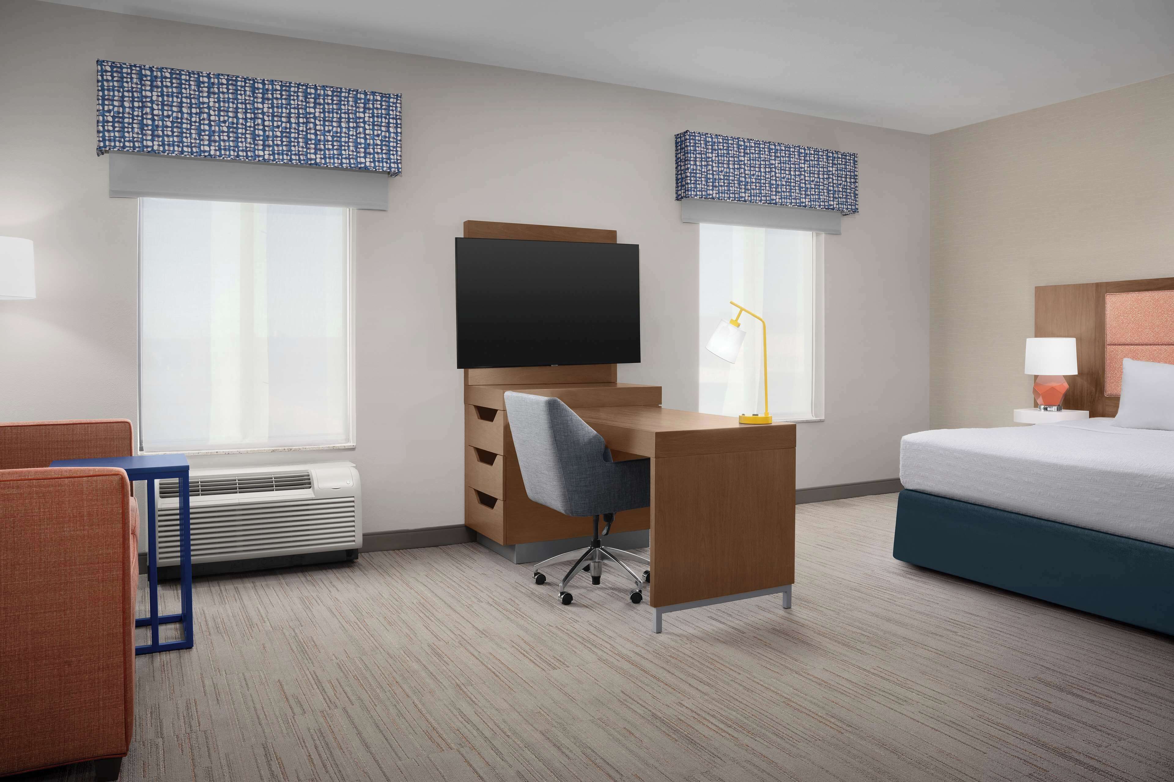 A hotel room with a bed, a desk with a chair, a television, and a window with a view.