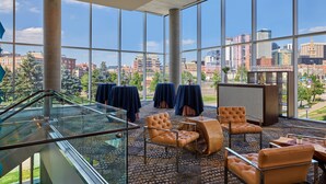 A spacious indoor area with large windows offering a city view, featuring leather chairs and tables, and a glass railing overlooking a lower level. - SpringHill Suites by Marriott Denver Downtown (Denver)