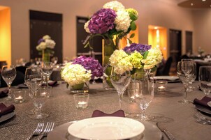 Una mesa de comedor dispuesta con cristalería, platos y servilletas, adornada con centros de mesa florales y velas.