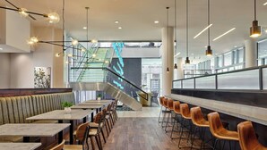 A modern restaurant with a long counter, wooden chairs, and a staircase leading to an upper level. - SpringHill Suites by Marriott Denver Downtown (Denver)