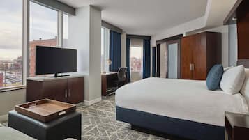 Ein Hotelzimmer mit einem großen Bett, einem Schreibtisch, einem Fernseher und Blick auf die Stadt.