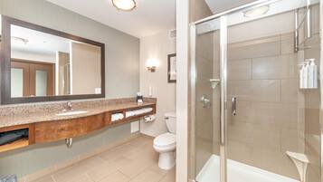 Een moderne badkamer met een granieten aanrecht, een toilet, een douche met glazen wanden en een grote spiegel.