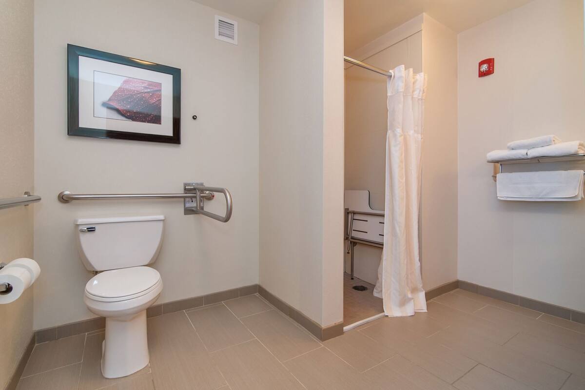 Une salle de bain équipée de toilettes, d’une barre d’appui, d’un rideau de douche et d’un porte-serviettes.