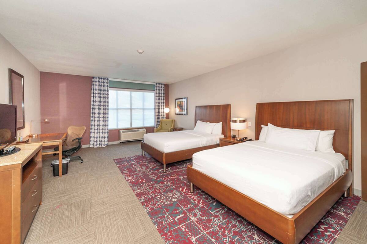 Une chambre d’hôtel avec deux lits, un bureau, une chaise, une télévision et une fenêtre avec des rideaux.