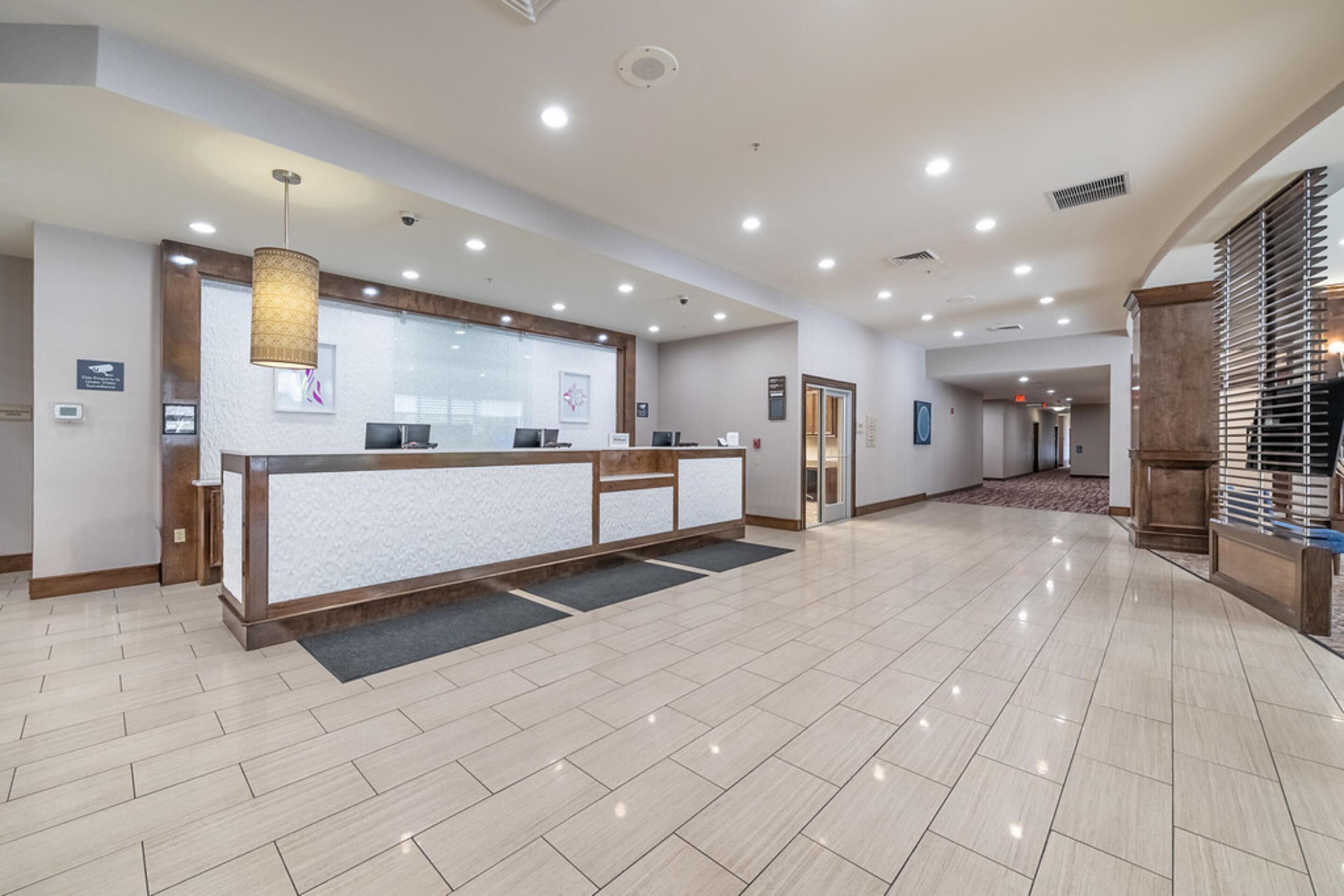 A hotel reception area with a reception desk, a hanging light fixture, and a tiled floor.