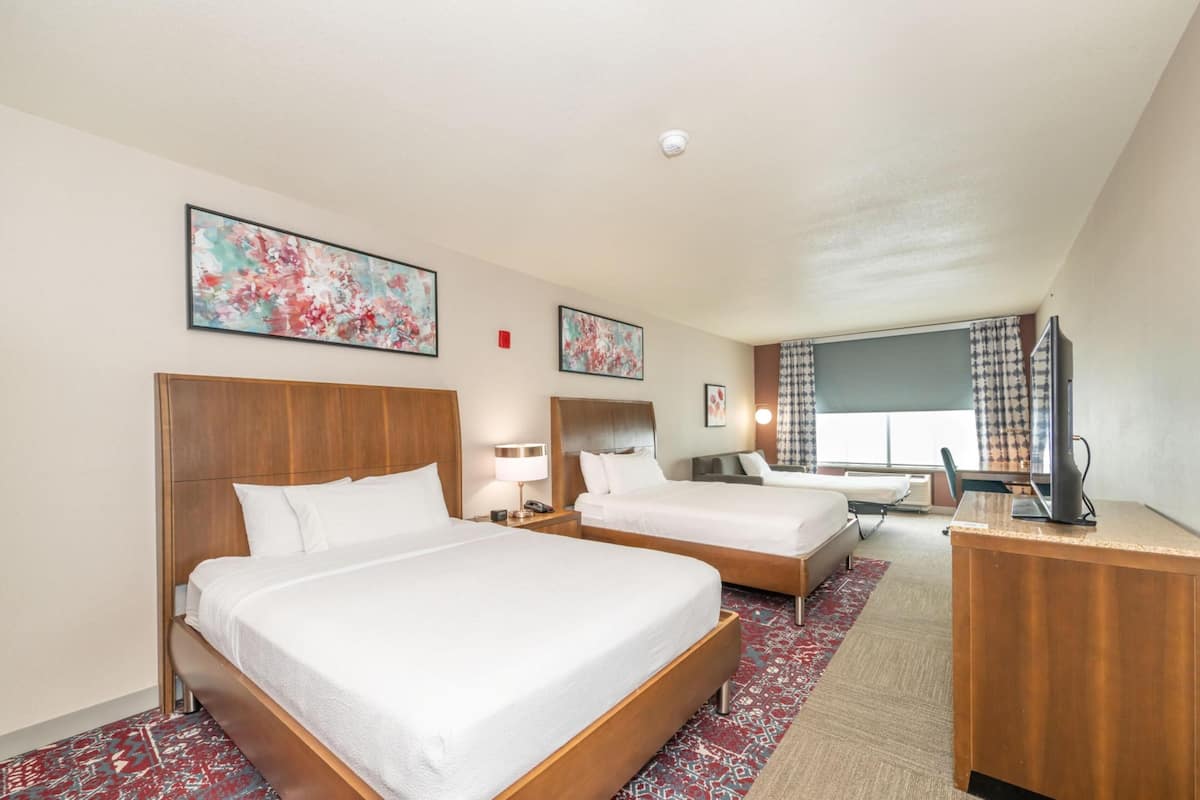 A hotel room with two beds, a desk, a TV, and artwork on the walls.