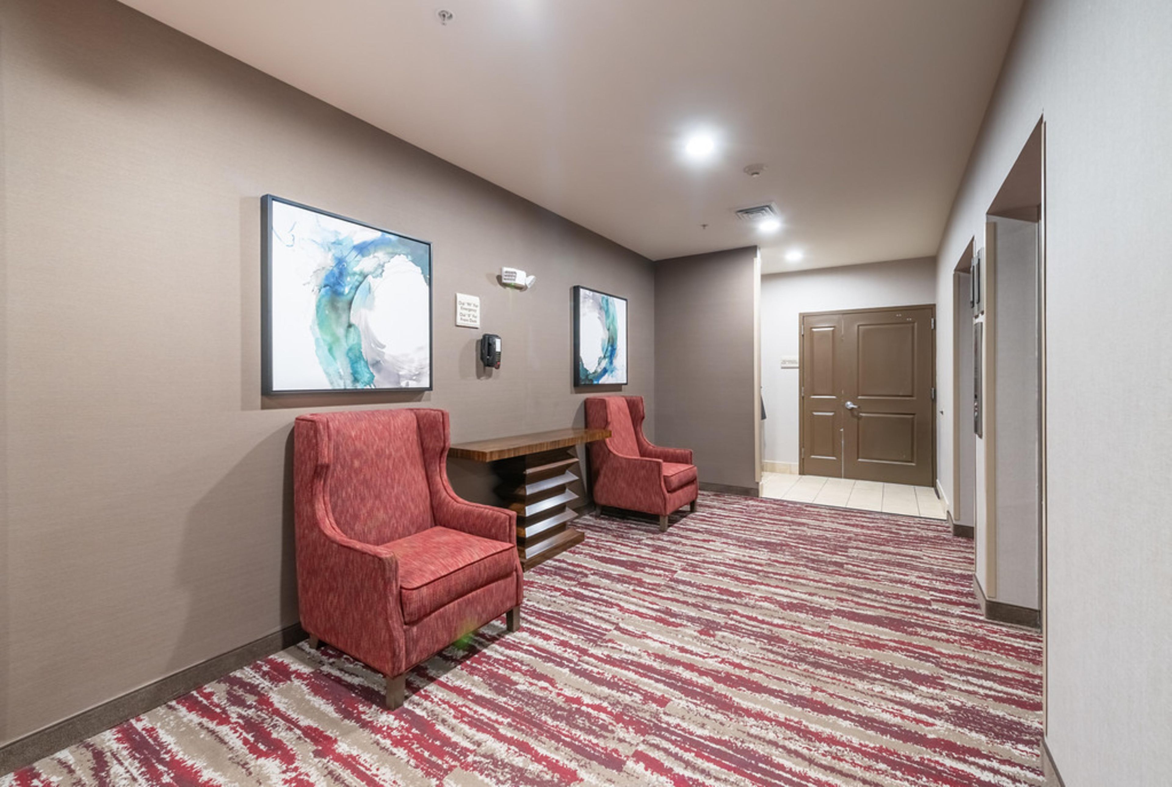 A hallway with two red armchairs, a wooden bench, and two abstract paintings on the wall.