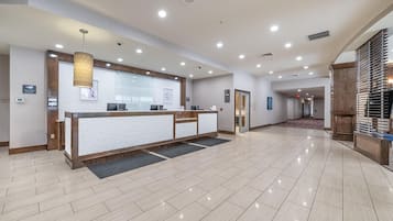 A hotel reception area with a reception desk, a hanging light fixture, and a tiled floor.