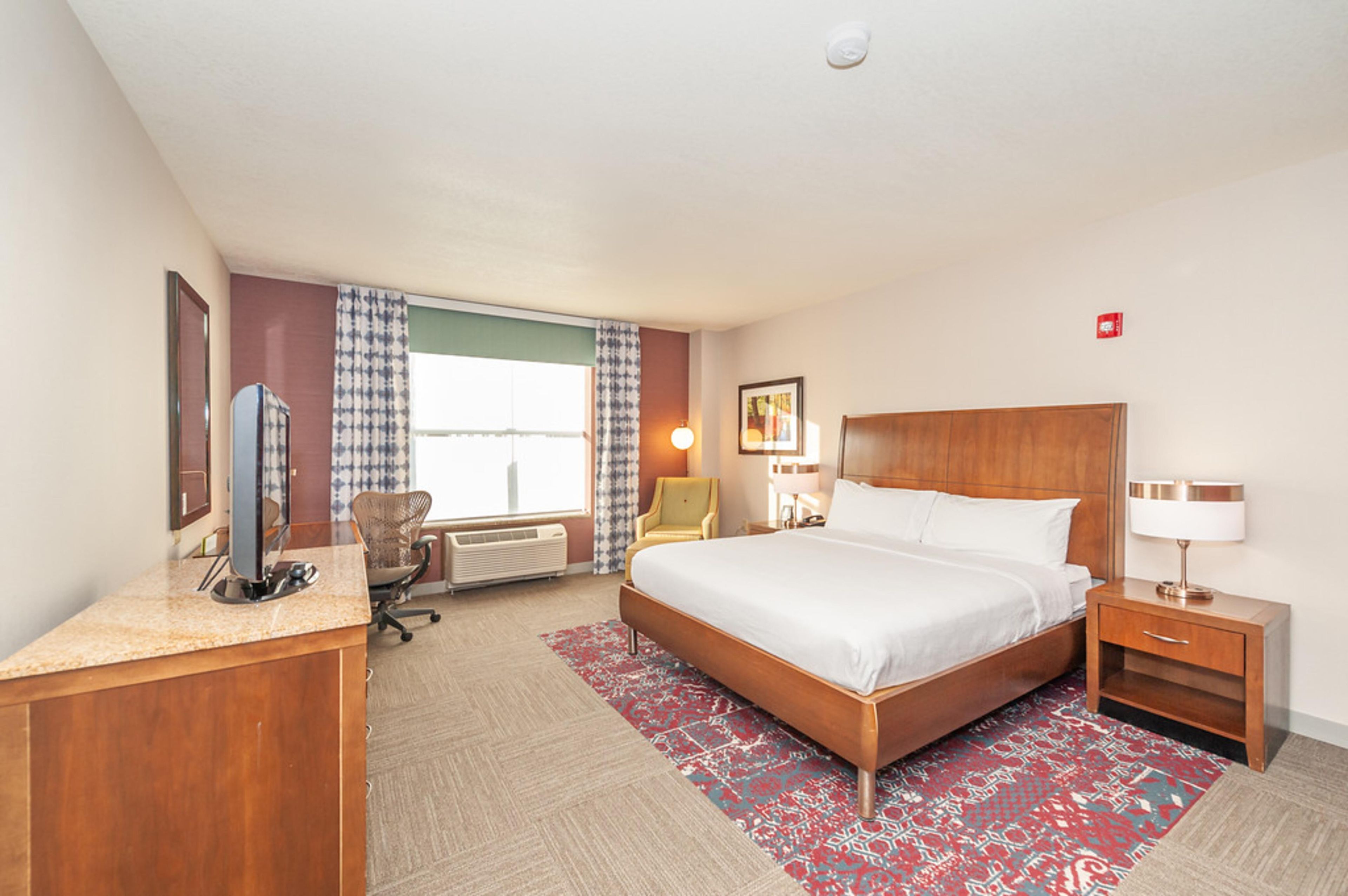 A hotel room with a bed, desk, chair, and a window with curtains.