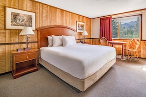 Habitación de hotel con una cama grande, dos mesitas de noche, un escritorio con una silla y una ventana con vistas a la montaña.