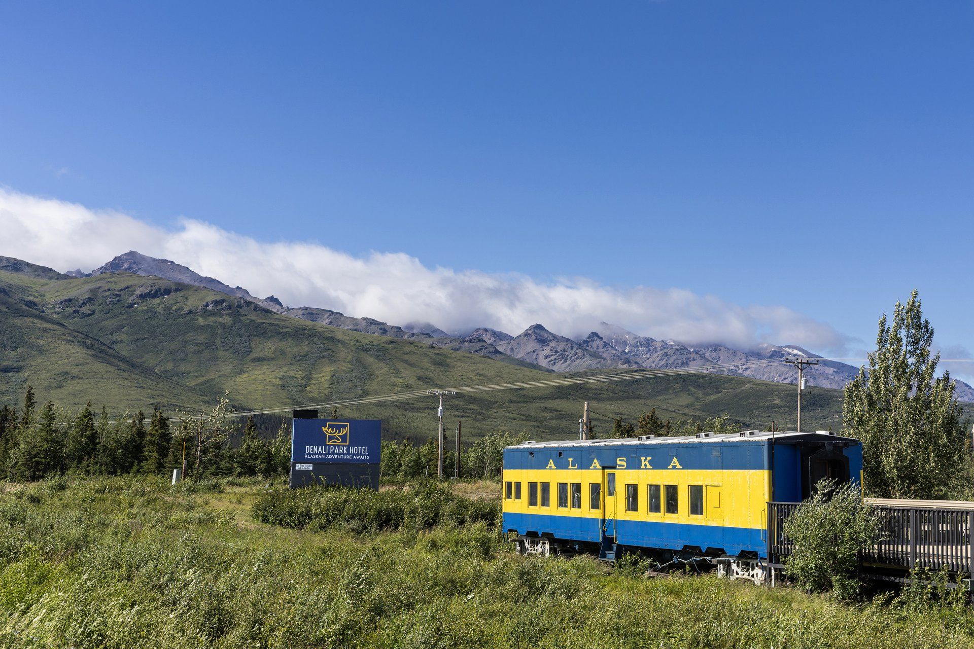 A train station with a sign for Denali Park Hotel and a blue and yellow train car.