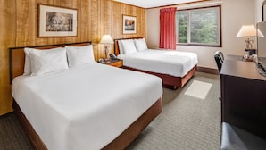 A hotel room with two beds, wooden paneling, a desk with a chair, and a window with a red curtain. - Denali Park Hotel (Healy)