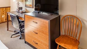A hotel room with a bed, a desk with a television, a chair, and a lamp.