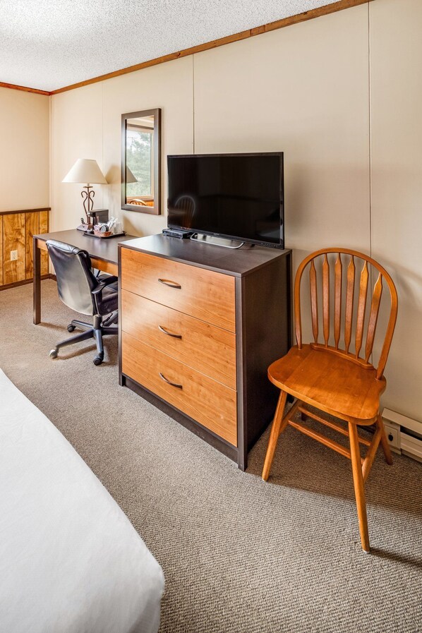 Una habitación de hotel con cama, escritorio con televisor, silla y lámpara.