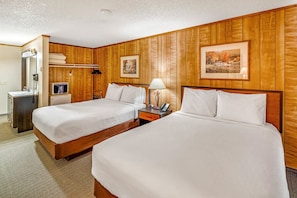 Habitación de hotel con dos camas, paneles de madera, un escritorio con lámpara, teléfono y un cuadro en la pared.