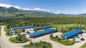 A lodge with multiple blue-roofed buildings, surrounded by dense forest and mountains. - Denali Park Hotel (Healy)