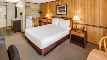 A hotel room with a bed, bedside tables, a desk, a chair, and a wooden wall panel.