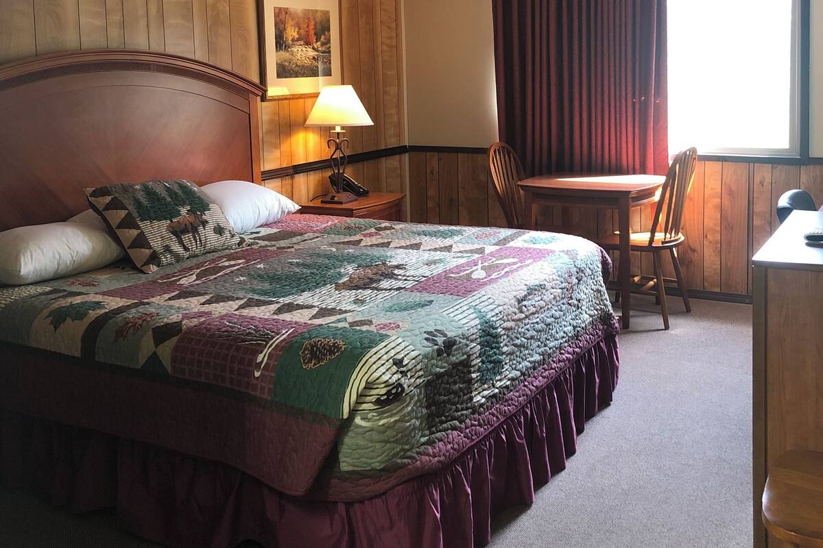 A hotel room with a large bed, a desk, a chair, a lamp, and a window with curtains.