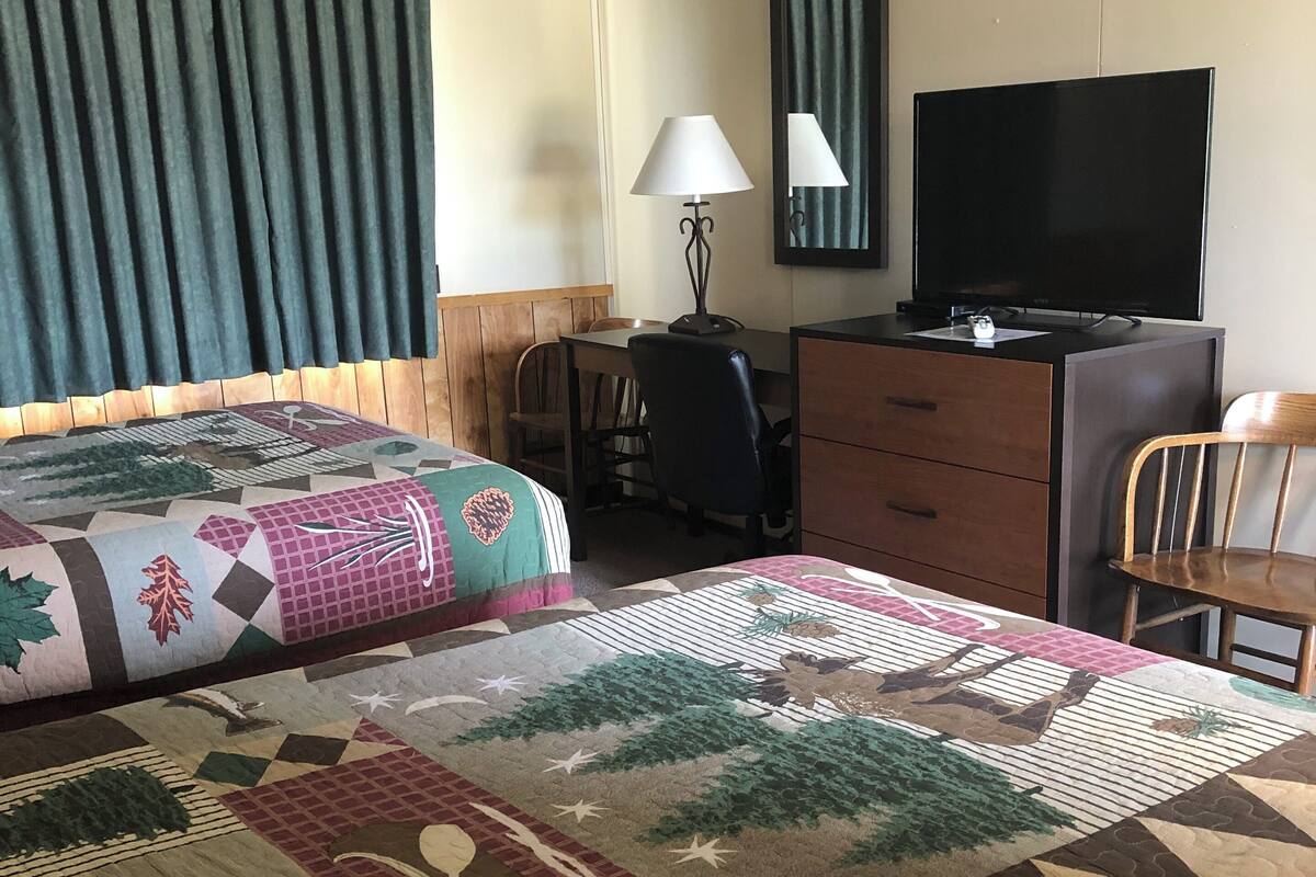 A hotel room with two beds, a desk, a chair, a television, and a lamp.