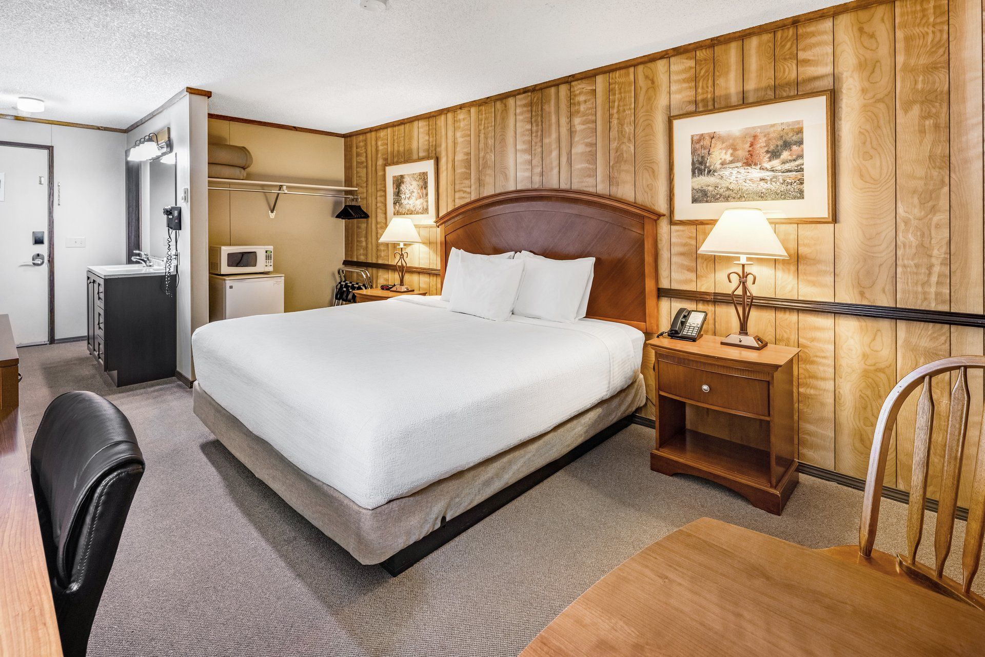 Een hotelkamer met een bed, nachtkastjes, een bureau, een stoel, een kapstok en een badkamer.