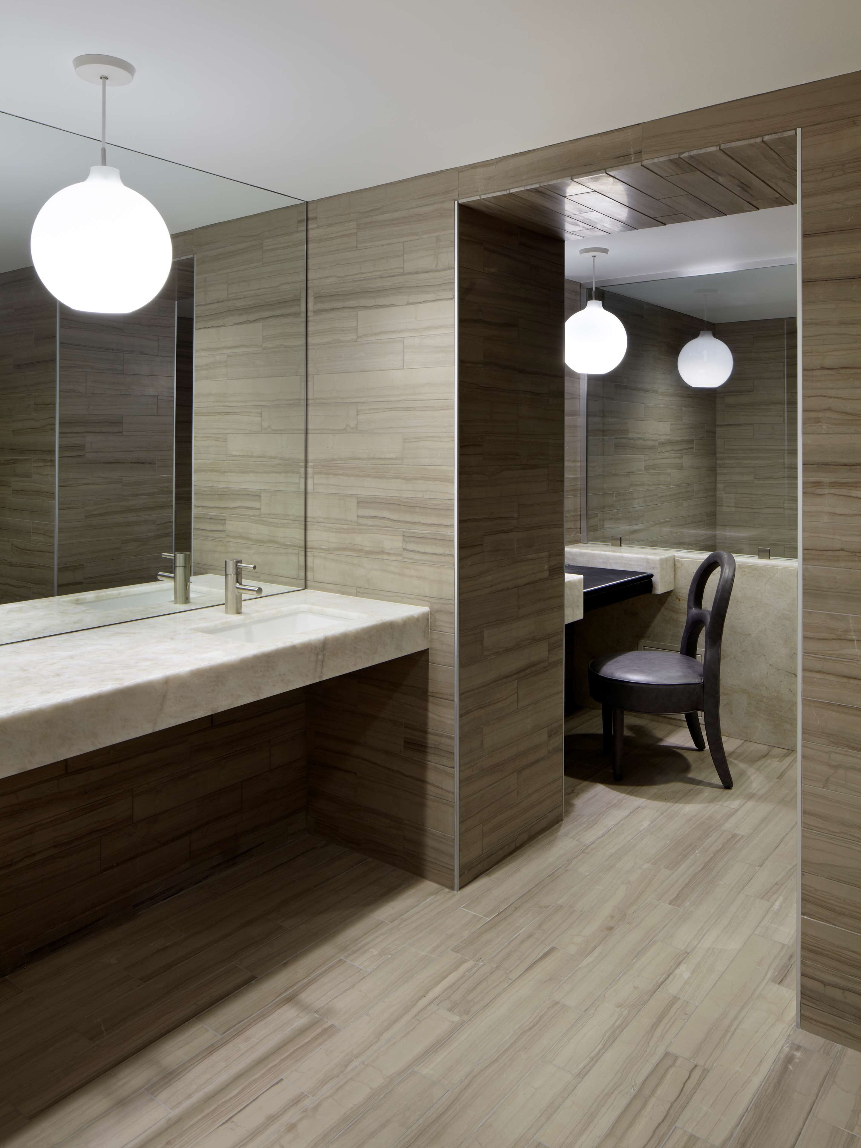 A modern bathroom with a large mirror, a sink, and a chair.