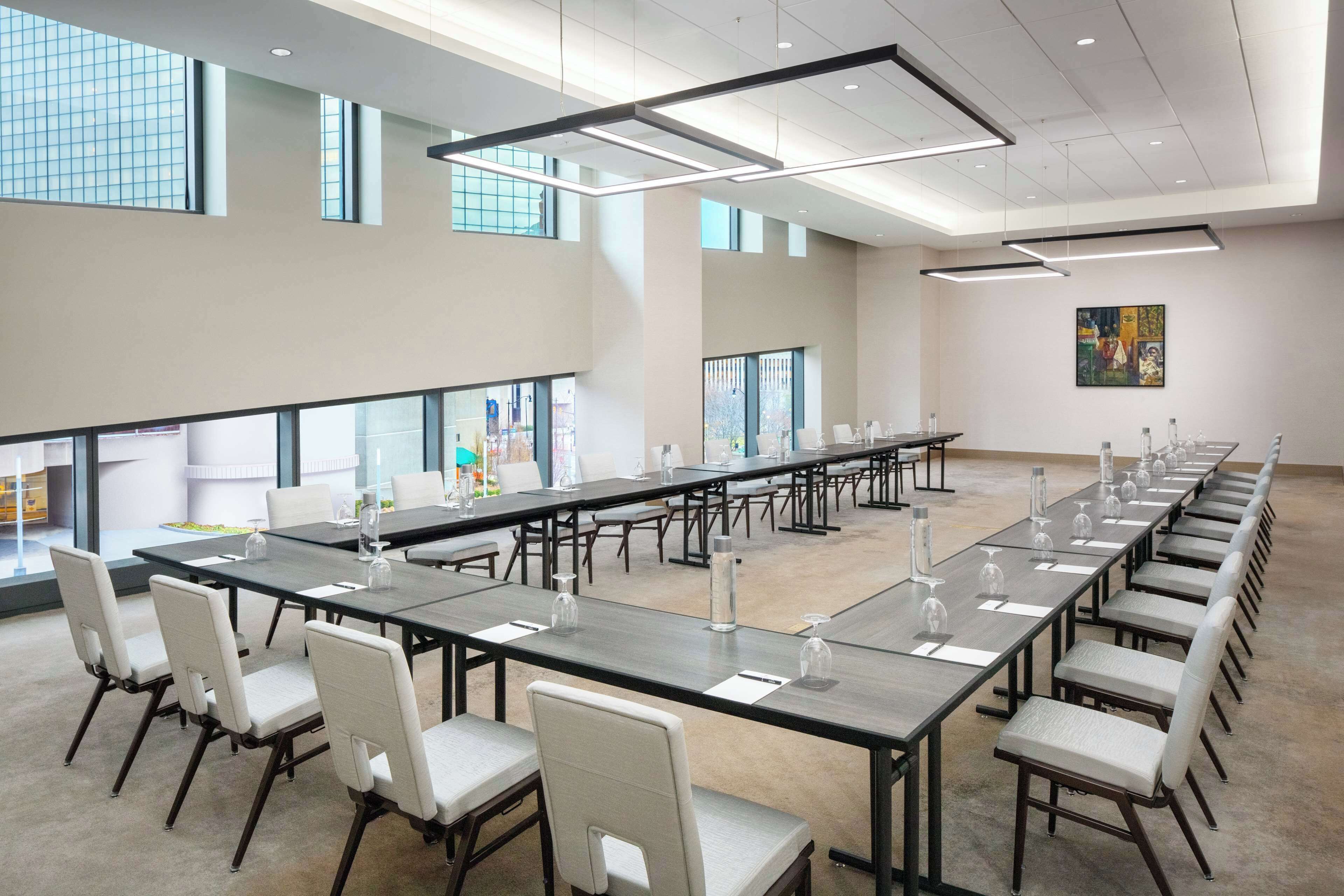 A conference room with long tables and chairs, large windows, and a modern ceiling design.