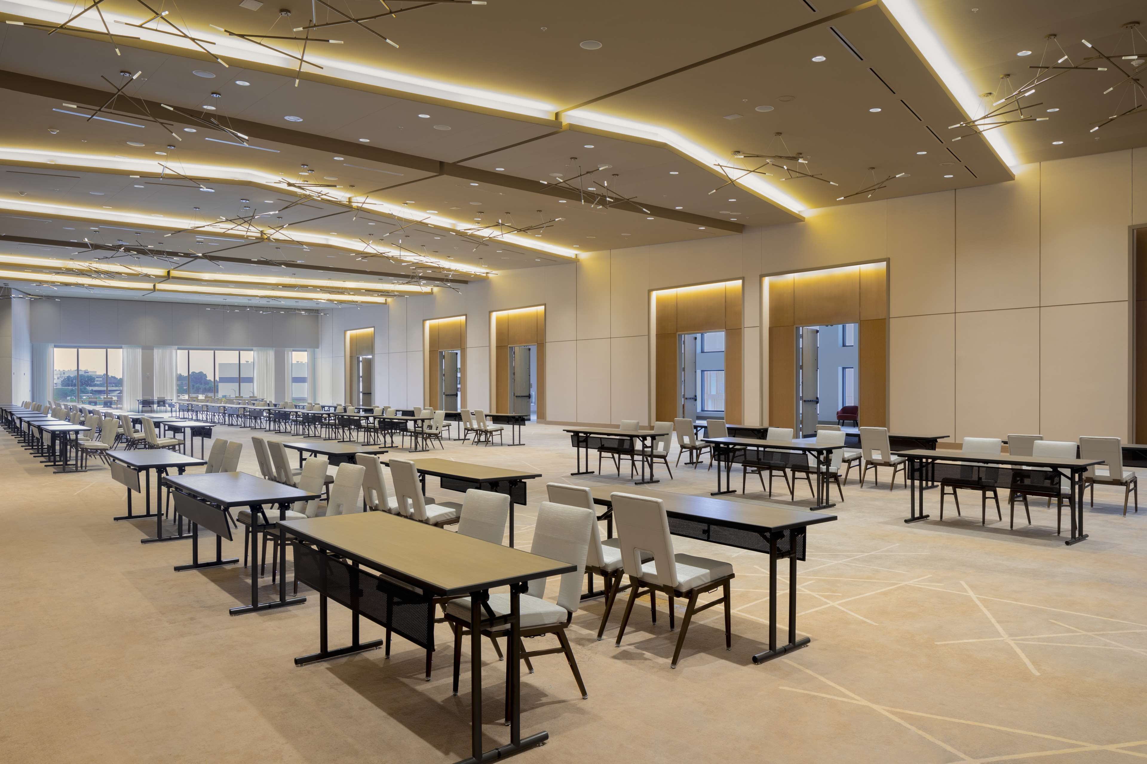 Une salle de conférence spacieuse, dotée de nombreuses tables et chaises, de grandes fenêtres et d’un éclairage moderne.