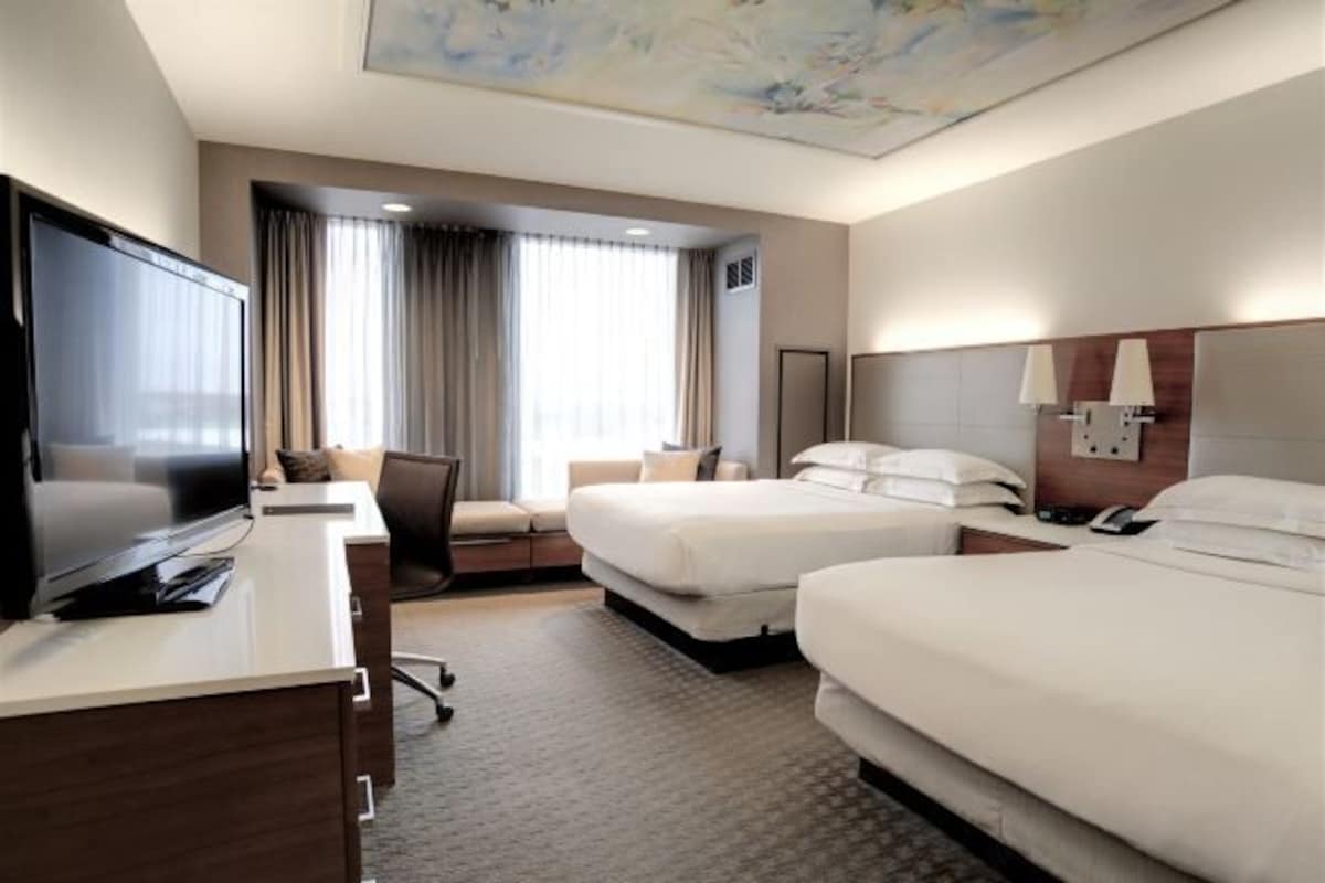 A hotel room with a large flat-screen TV, two beds, a desk, and a chair.