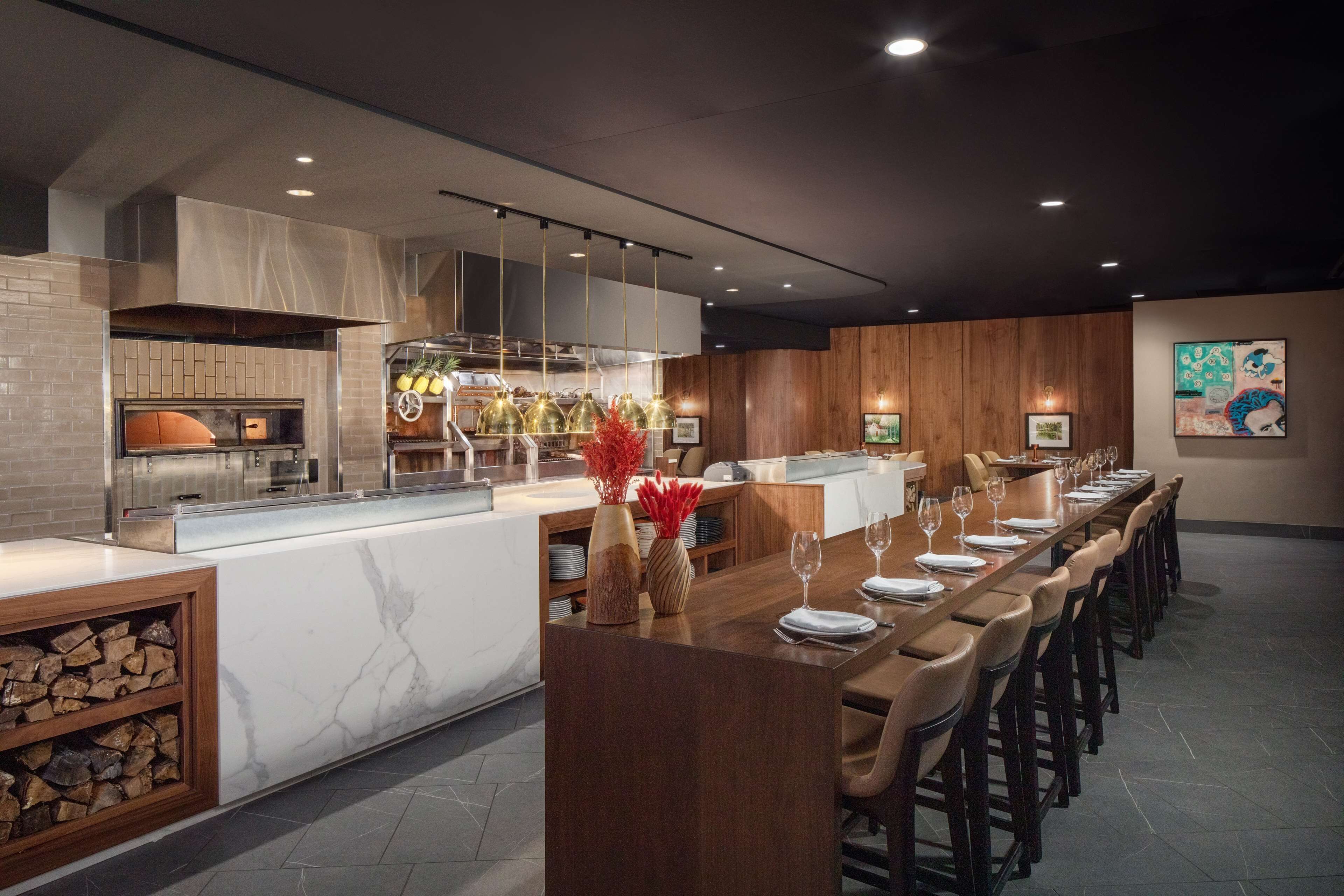 A modern restaurant with a long dining table, wooden chairs, and a marble countertop.