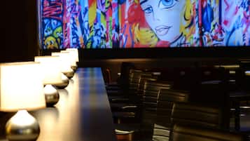 A bar area with a long counter, multiple illuminated lamps, and a large screen displaying a colorful abstract painting.