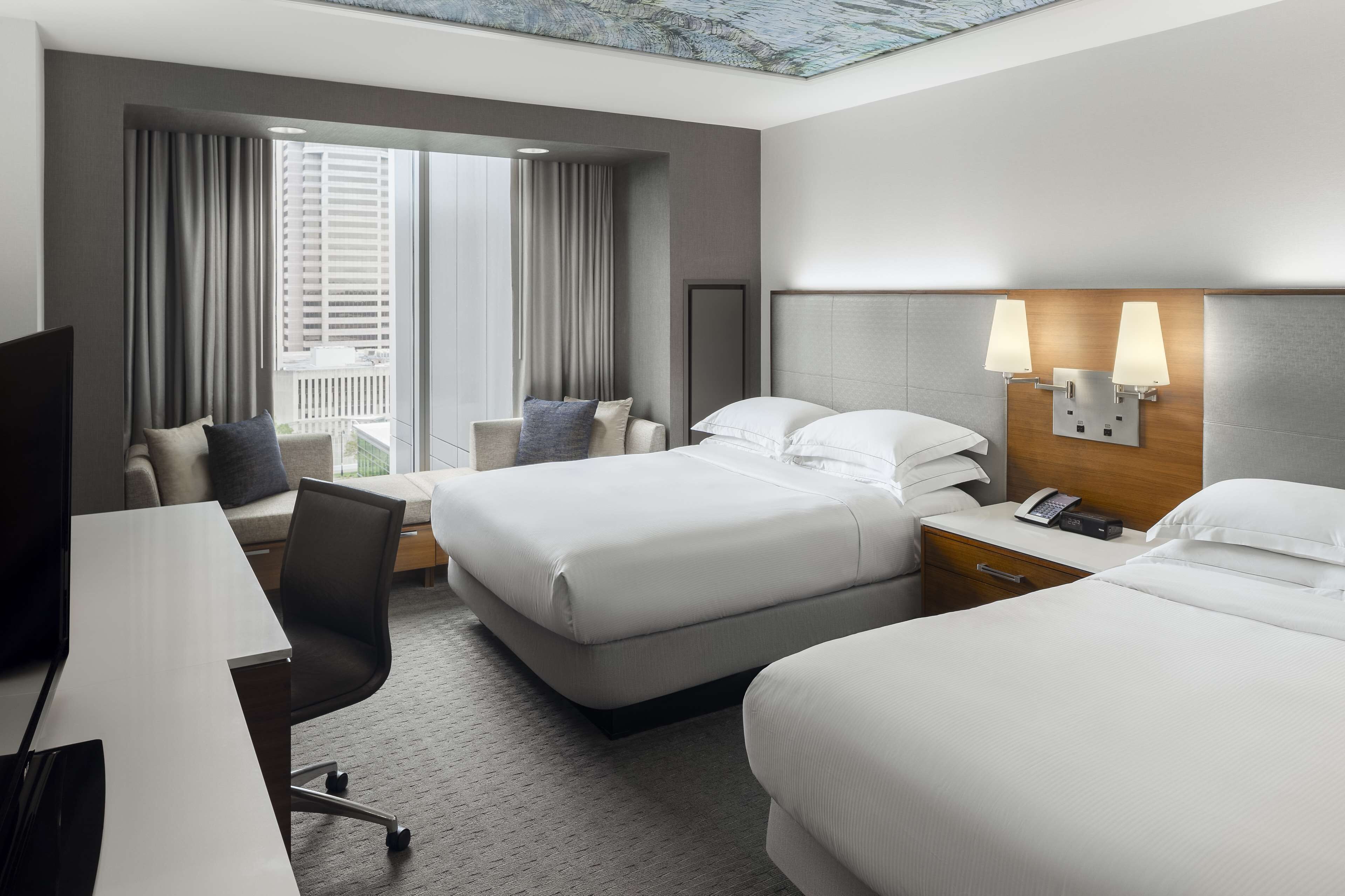 A hotel room with two beds, a desk, a chair, a TV, and a balcony with curtains.