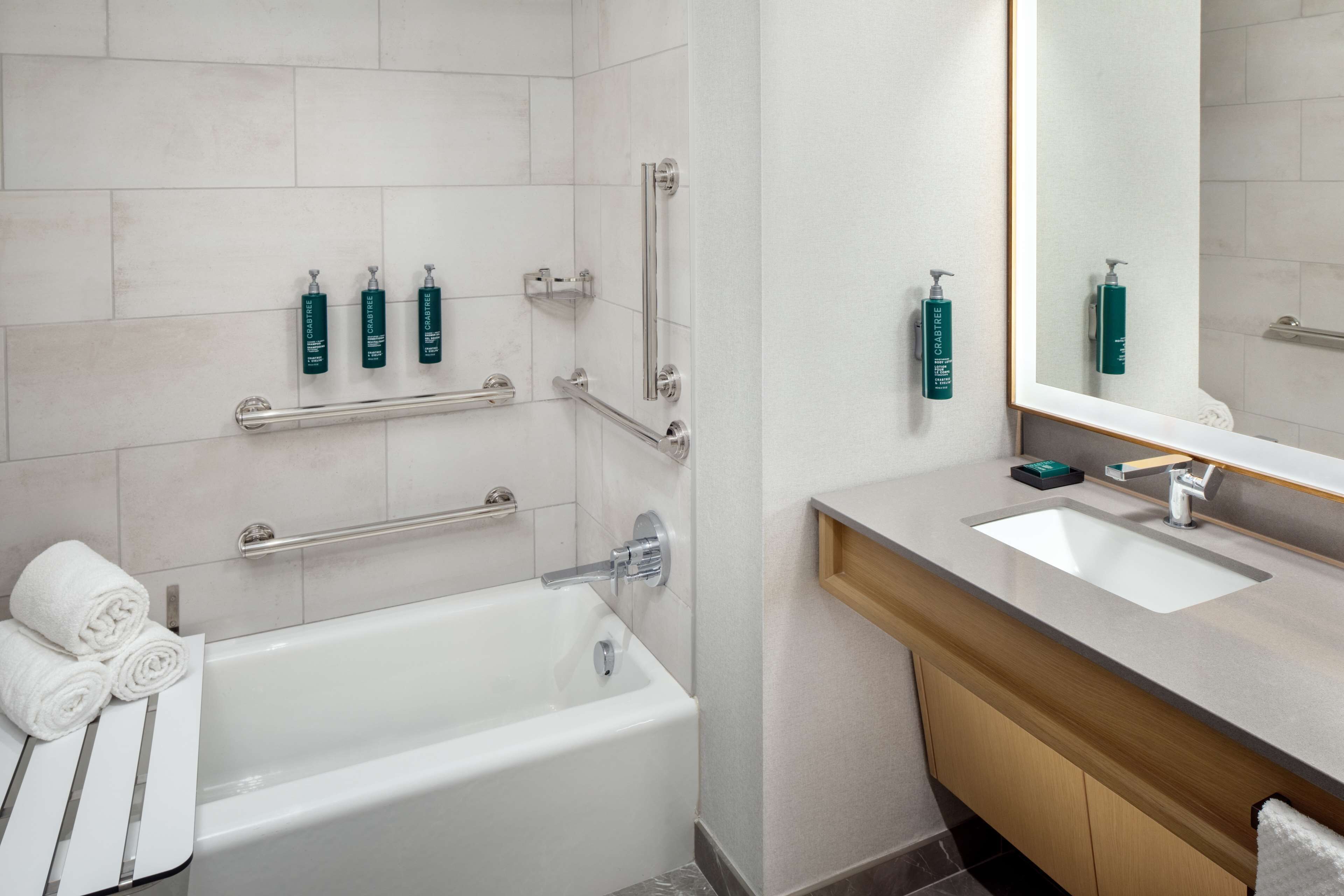 A modern bathroom with a bathtub, a vanity with a sink, and handrails.