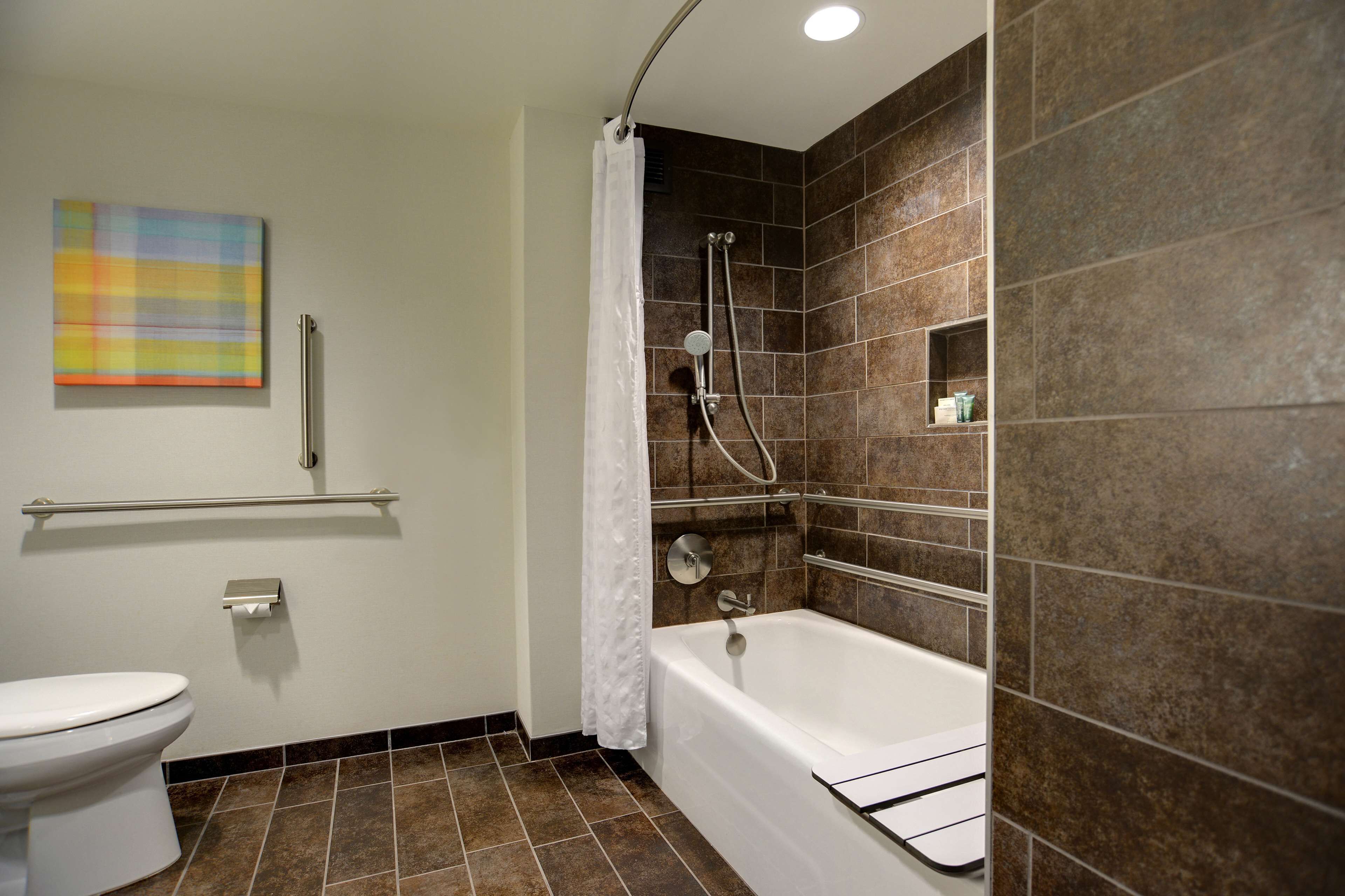 A bathroom with a bathtub, a toilet, and a shower with a handrail.